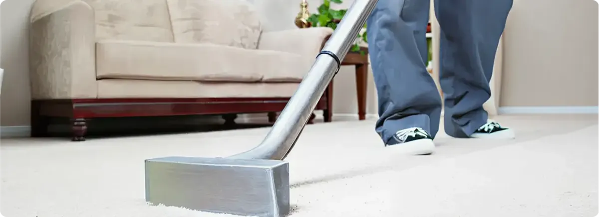 Carpet cleaning technician using a hot-water extraction wand on a light-colored carpet in a living room, Des Moines, IA.