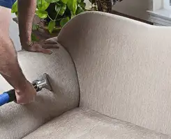 Professional upholstery cleaner deep-cleaning a fabric sofa with a handheld extraction tool and hose in Des Moines, IA.